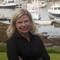 Photo of Professor Diane Lebson standing on a waterfront with fishing boats in the background