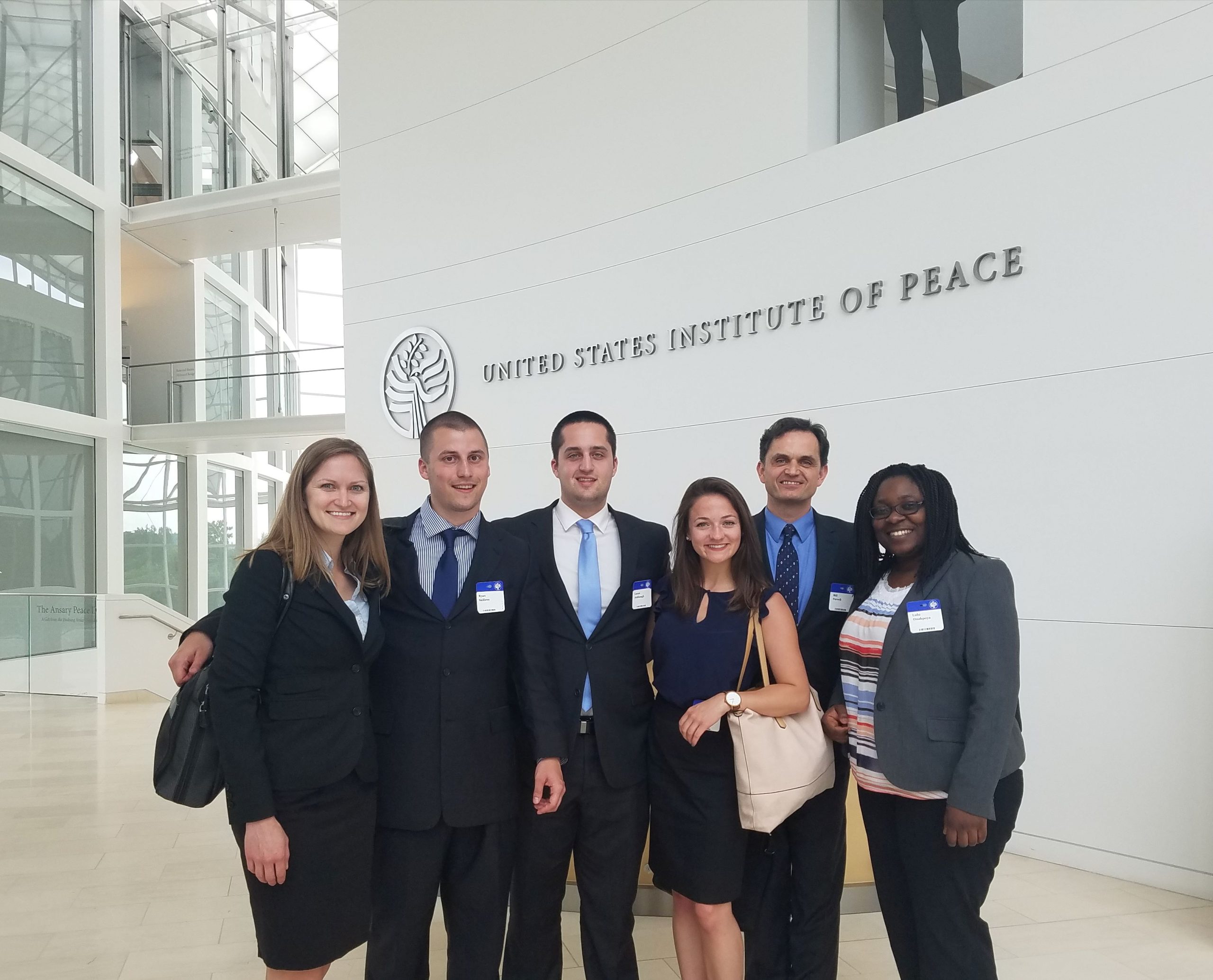 Group of professionally dressed students posing for a photo in the lobby of the US Institute of Peace in Washington, DC